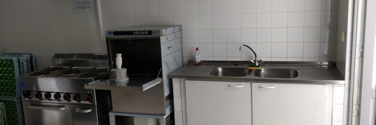Cuisine avec plaque de cuisson, hotte, lave-vaisselle, évier, robinet et étagères.