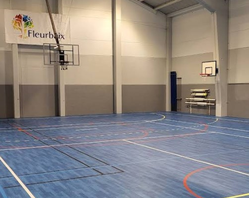 Salle de sport avec panier de basket, filet, échelle et sol bleu.