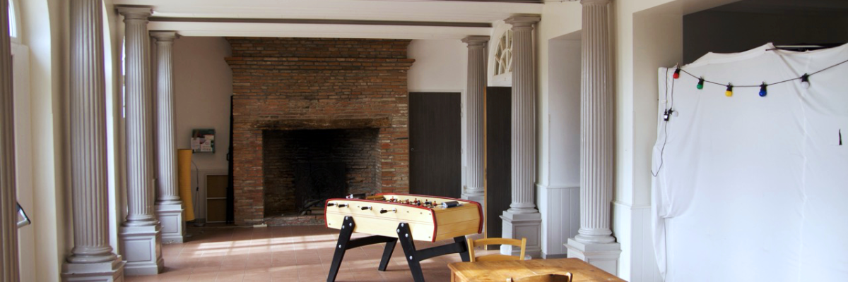 Pièce avec colonnes, cheminée, table de football, table et chaises.