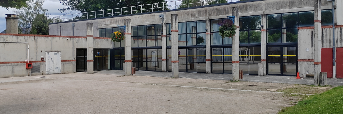 Bâtiment industriel avec grandes portes, fenêtres et parking en gravier.