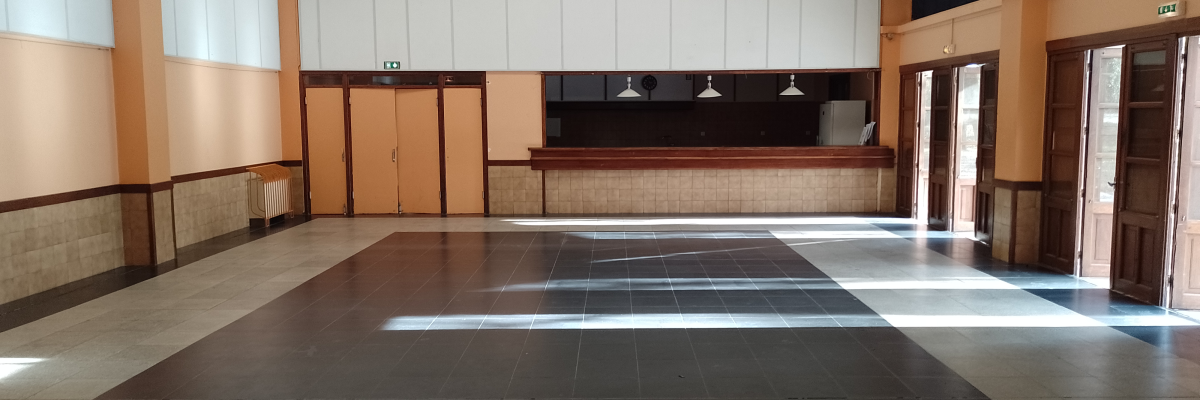 Salle vide avec parquet, comptoir, lustres, portes et fenêtres.