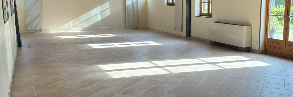 Salle vide avec poutres apparentes, fenêtres et porte.