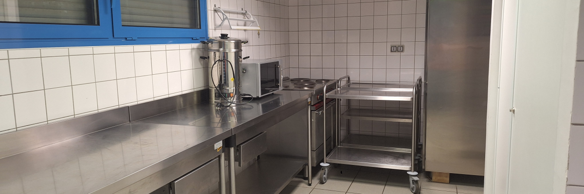 Cuisine avec comptoir en acier inoxydable, chariots, micro-ondes, plaque de cuisson, hotte et réfrigérateur.