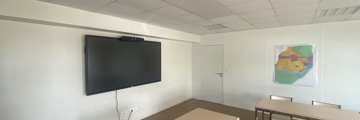 Salle avec télévision, tables, chaises et tableau blanc.