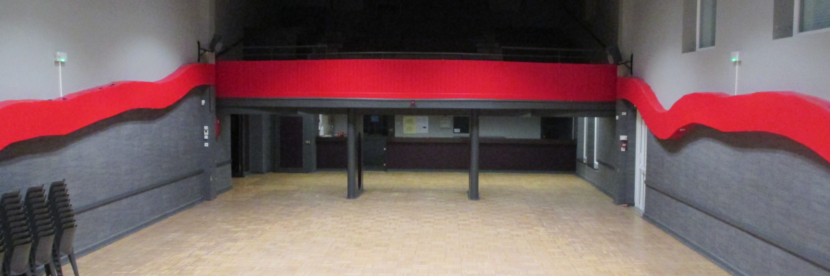 Salle avec estrade, chaises empilées, éclairage et décorations murales rouges.
