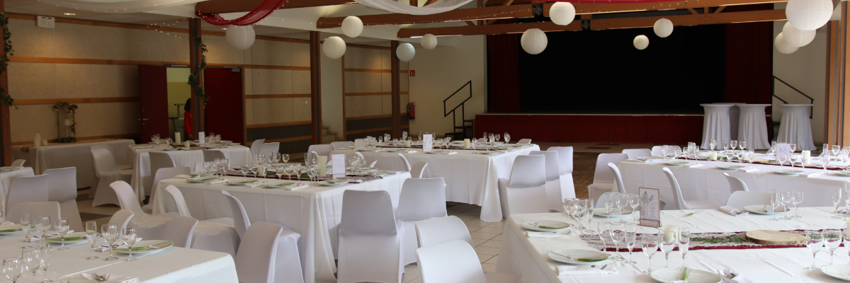 Salle avec tables, chaises, nappes, verres, vaisselle et décorations suspendues.