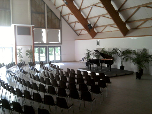 Salle avec chaises, piano, plantes et structure en bois.