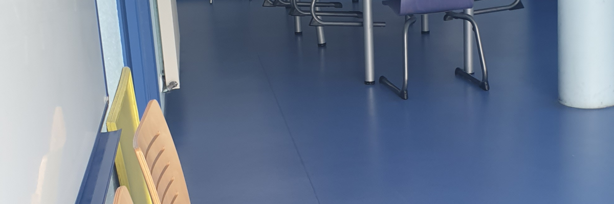 Salle bleue avec tables, chaises, ordinateurs et armoires.