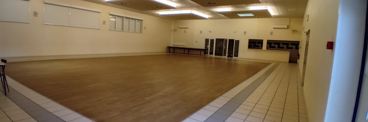 Salle vide avec parquet, murs blancs, éclairage encastré, fenêtres, bancs et portes.