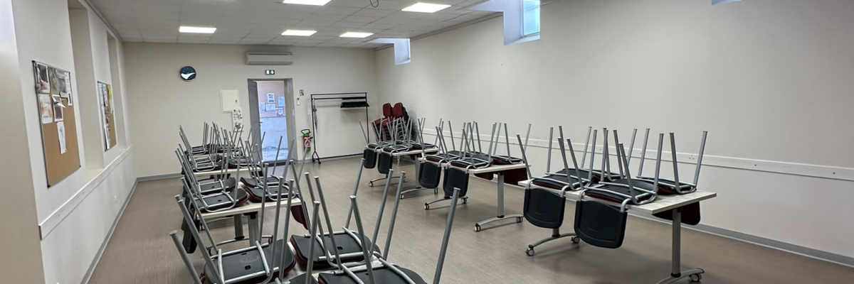 Salle avec tables, chaises, projecteur, écran et ordinateurs.