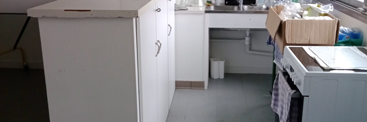 Laboratoire avec paillasse, micro-ondes, ordinateur, meubles, poubelle et étagères.