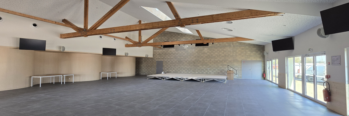 Salle avec poutres en bois, écrans, tables pliables et rangées contre le mur.