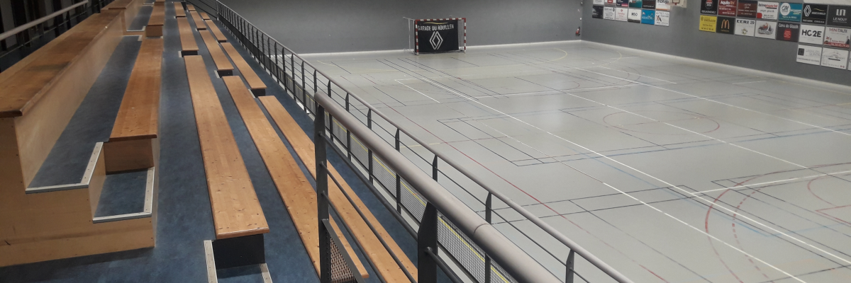 Patinoire avec gradins, surface de glace, filet et panneaux publicitaires.