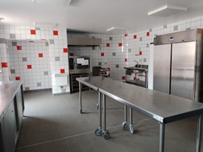 Cuisine industrielle avec plans de travail en inox, frigo, plaques de cuisson et étagères.