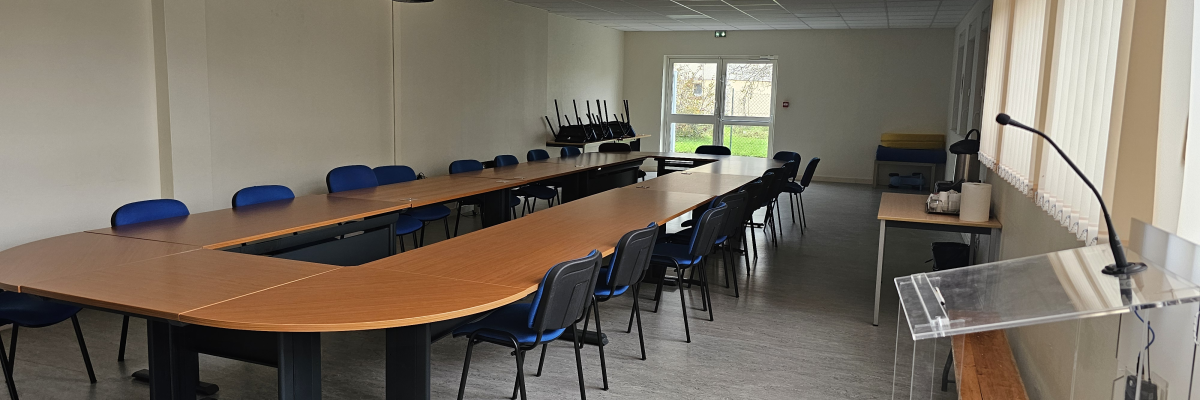 Salle avec tables en forme de U, chaises, video projecteur, écran et pupitre.