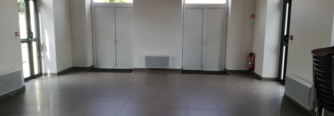 Salle vide avec portes, fenêtres, radiateurs, extincteur et chaises.