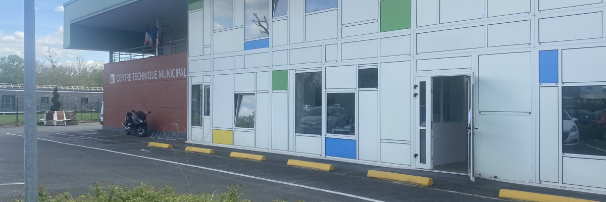Bâtiment avec panneaux colorés, fenêtres et porte en verre. Panneau indiquant "Centre Technique Municipal". Motos stationnées devant.