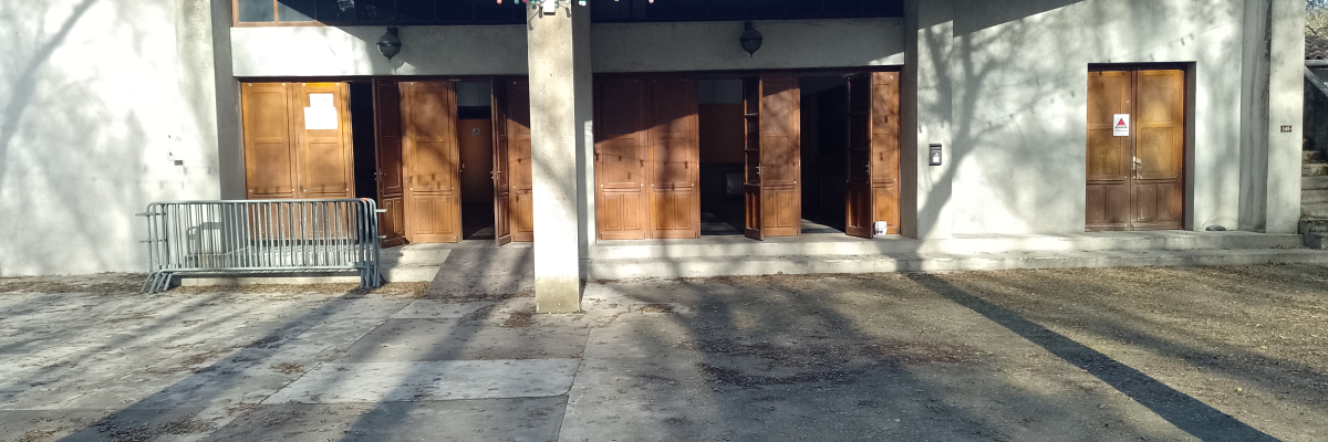 Bâtiment avec portes en bois, toit en tuiles, sol en gravier, rampes, et guirlandes lumineuses.