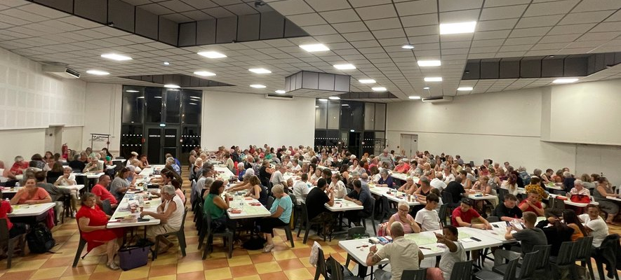 Salle de cantine avec tables, chaises, et personnes mangeant.