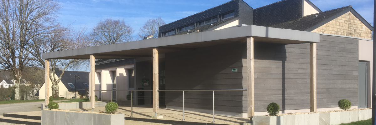 Bâtiment moderne avec colonnes, toit plat, entrées vitrées et allée gravillonnée.