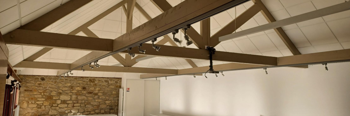 Salle avec poutres apparentes, tables, chaises et mur en pierre.