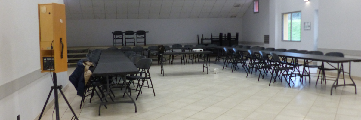 Salle avec tables, chaises, projecteur, trépied et climatiseurs.