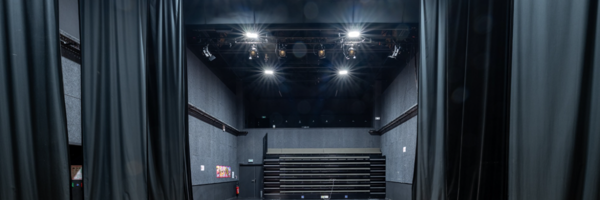 Salle de spectacle avec scène, projecteurs, rideaux et gradins.