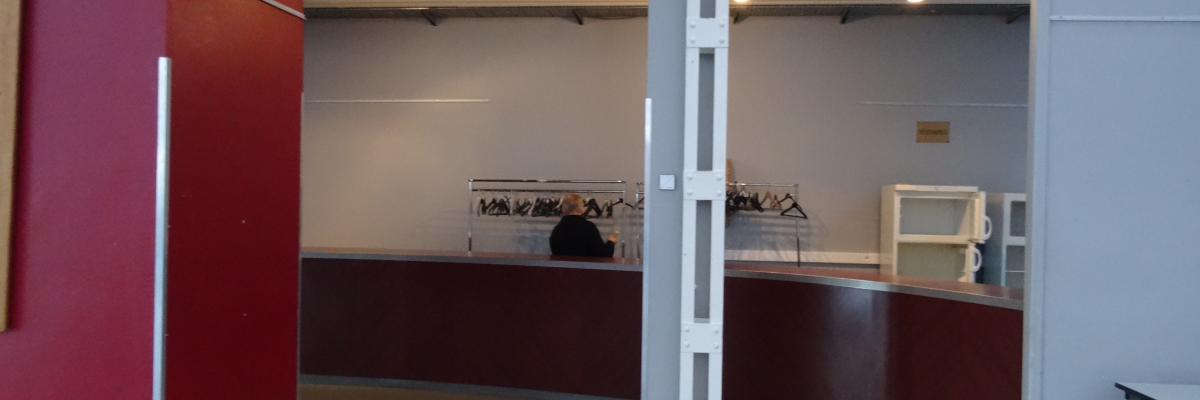 Espace d'exposition avec murs rouges, comptoir, étagères, et banc.