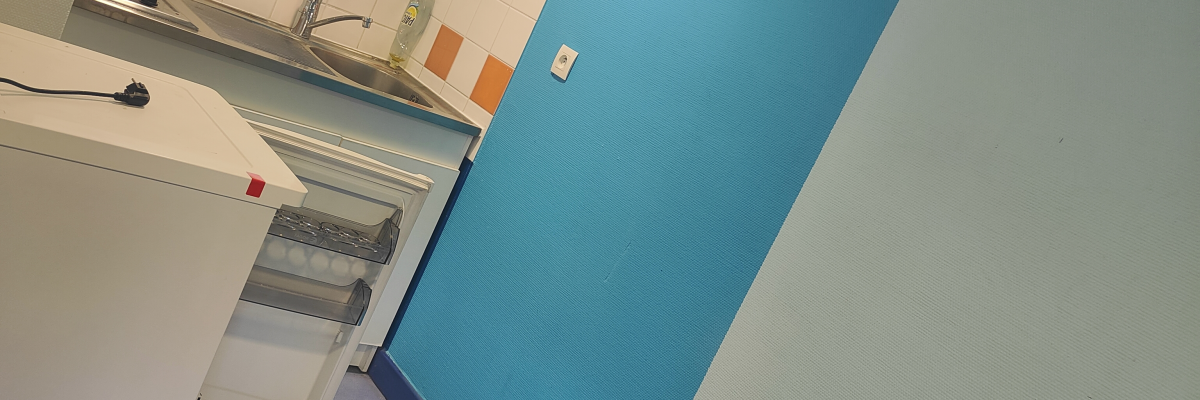 Pièce avec meuble de rangement, table, distributeur de papier, mur bleu et blanc, sol gris.