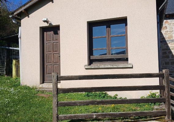 Maison avec porte en bois, fenêtre, clôture en bois et terrain herbeux.