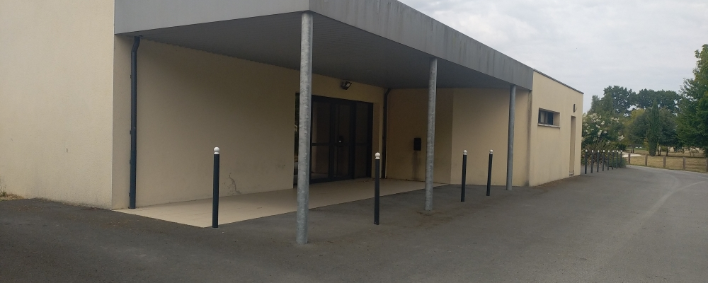 Bâtiment beige avec auvent, portes et poteaux.