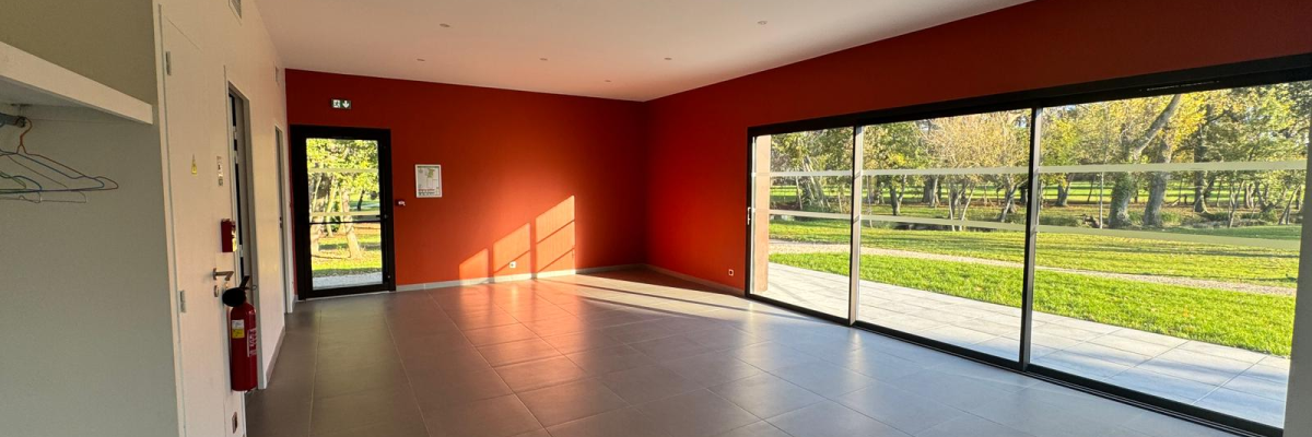 Pièce vide avec murs rouges, sol gris, grandes baies vitrées, porte et placard.