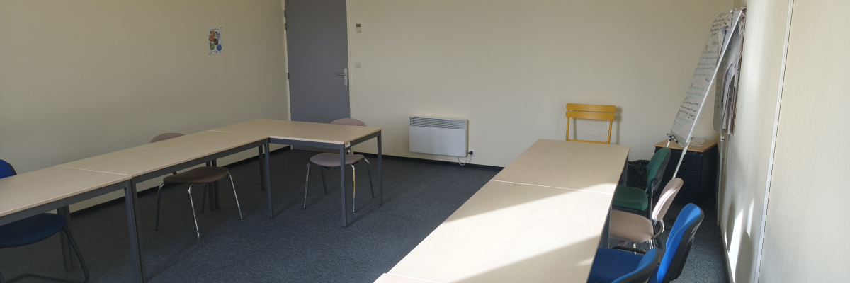 Salle avec table, chaises, tableau blanc, éclairage et unité de climatisation.