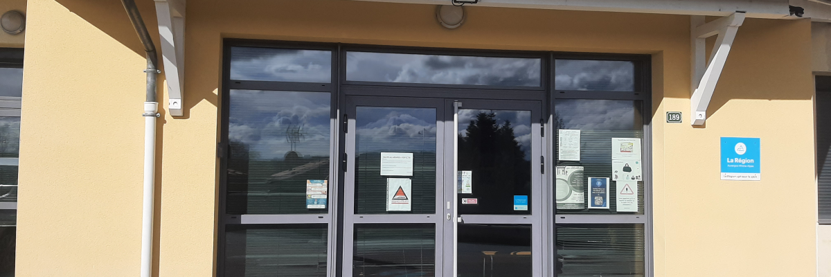 Entrée de bâtiment avec portes vitrées, auvent et panneaux d'affichage.