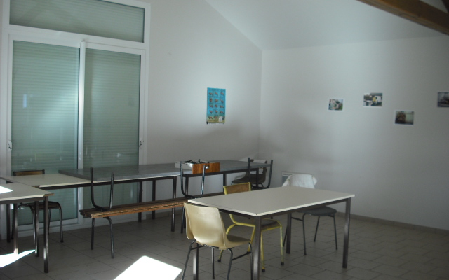 Salle avec tables, chaises, tableau d'affichage et fenêtres.
