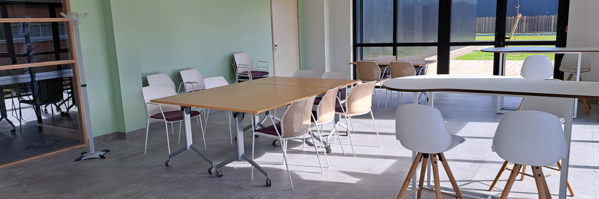 Salle avec tables, chaises, étagères, luminaires muraux et fenêtre.