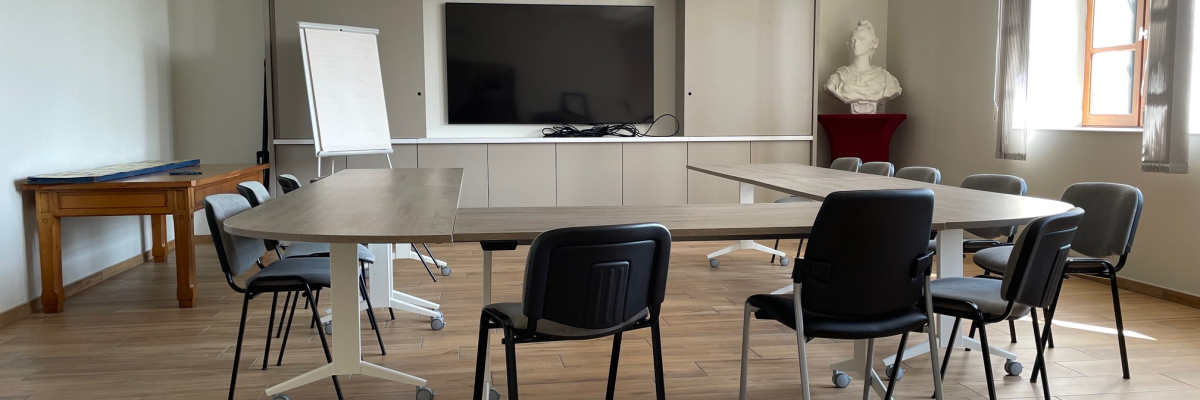 Salle avec table, chaises, tableau blanc, télévision et bureau.