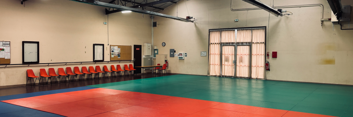 Salle avec tapis de combat, chaises, table et portes.