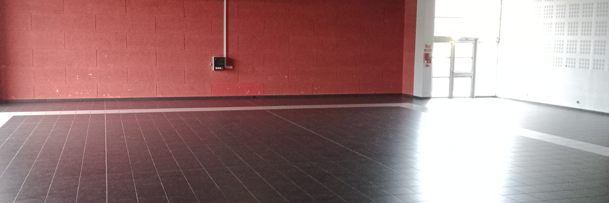 Salle vide avec sol noir, mur rouge, projecteurs au plafond.