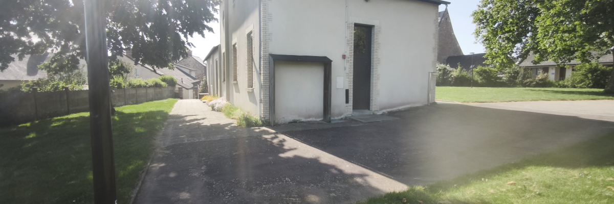 Bâtiment blanc avec toit gris, allée, pelouse, arbres et poteau.