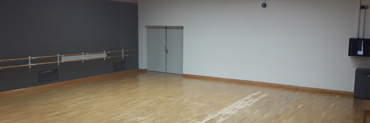 Salle avec parquet, barre de danse, porte, climatiseur et lumières.