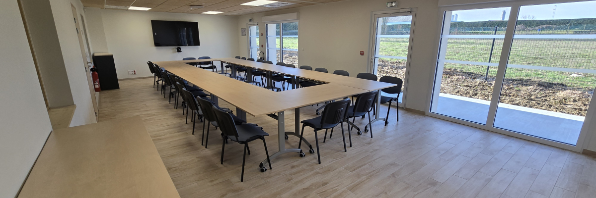 Salle avec table, chaises, écran, porte, fenêtres, meuble et extincteur.