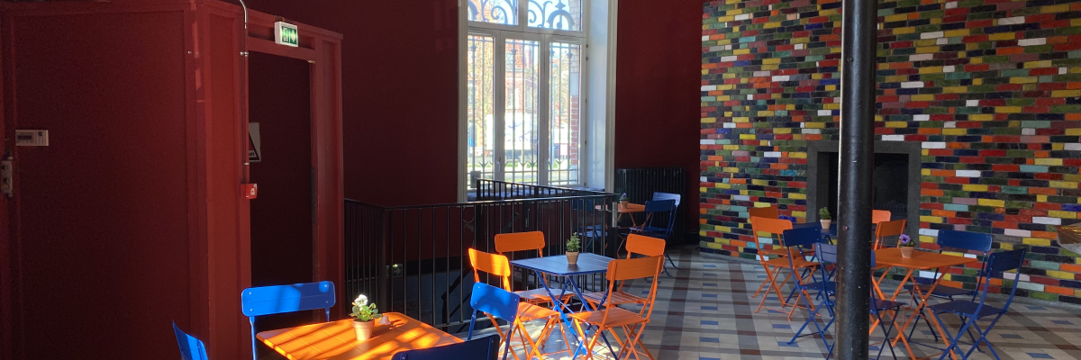 "Salle avec tables, chaises, et porte rouge. Carrelage coloré au sol et murs."