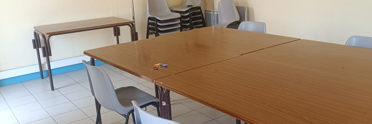 Salle avec table, chaises, étagère et climatiseur mural.