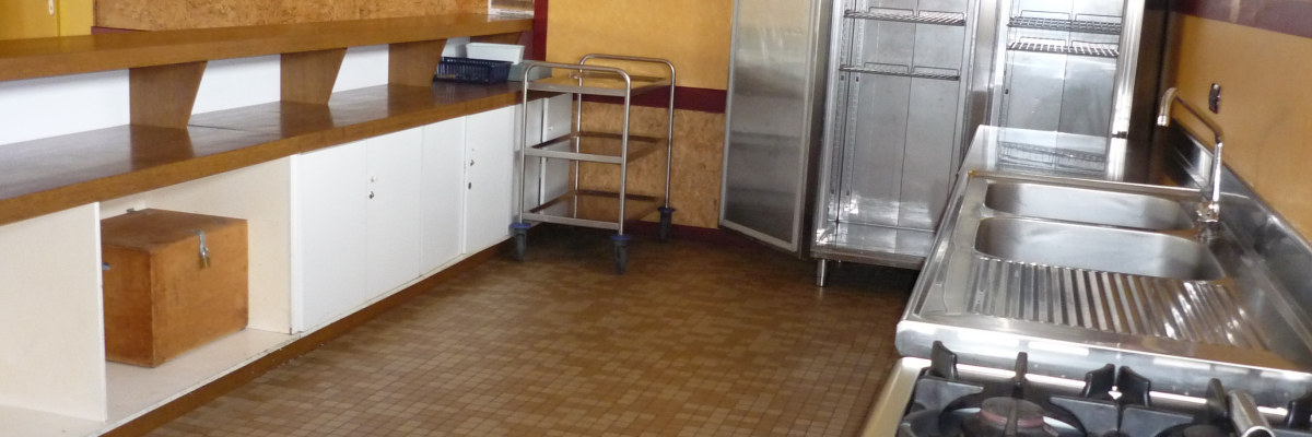 Cuisine avec plans de travail, chariot, réfrigérateurs, évier et cuisinière à gaz.