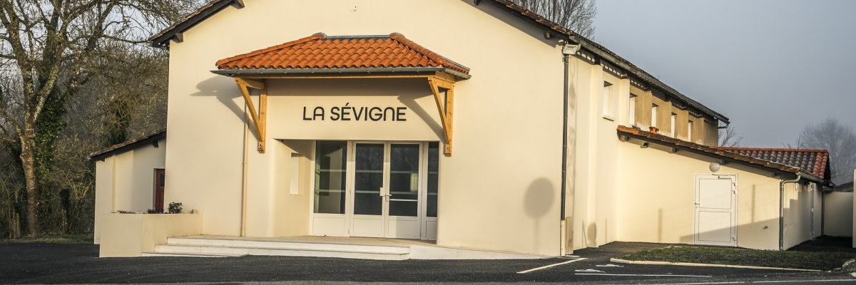 Bâtiment jaune avec toit en tuiles orange, entrée encadrée par deux portes vitrées et un auvent.