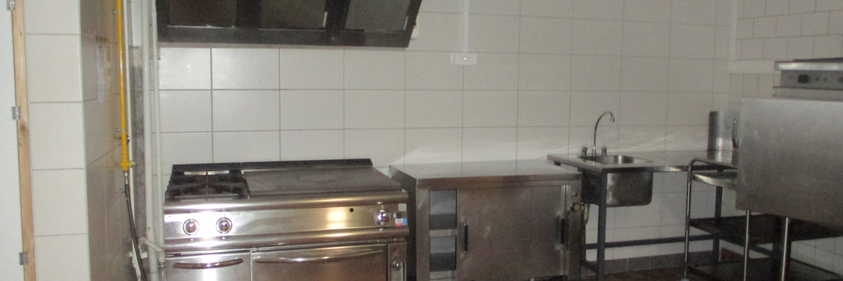 Cuisine avec plaque de cuisson, four, hotte, évier, plan de travail et étagère métallique.