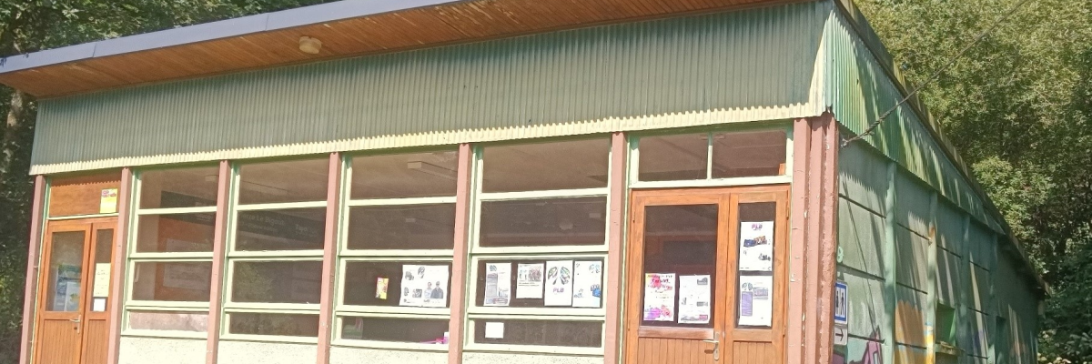 Bâtiment avec toiture en bois, murs métalliques, grandes fenêtres et portes en bois. Affiches aux fenêtres.