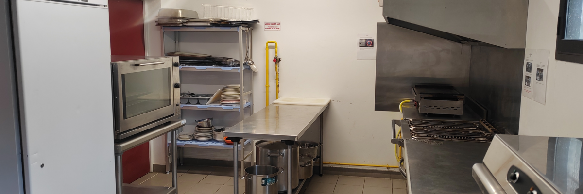 Cuisine professionnelle avec frigo, four, étagères, plan de travail, hotte, et divers équipements.