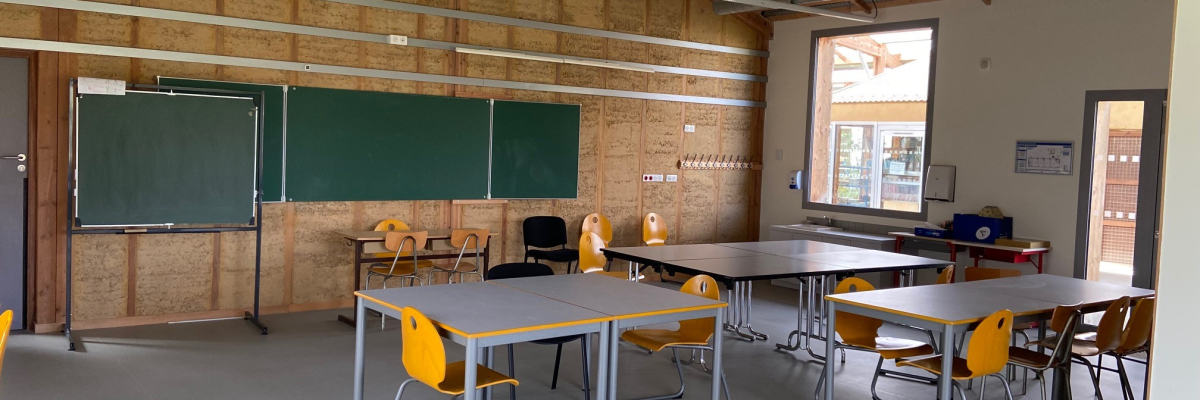Classe avec tables, chaises, tableau, porte-manteau et matériel pédagogique.
